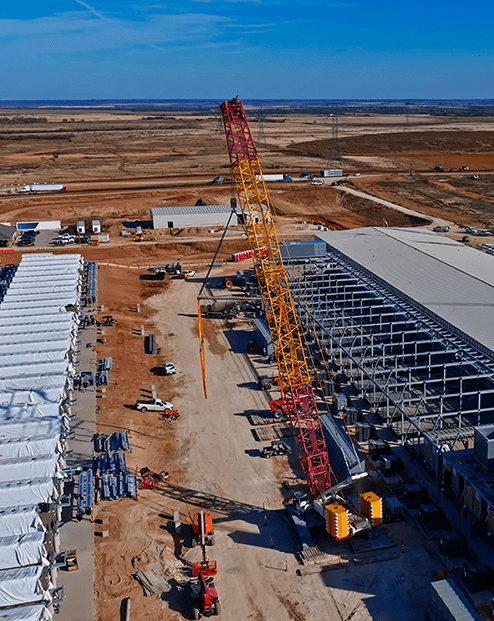 Aerial construction view shows data center structures BESS batteries red cranes and metal framing.