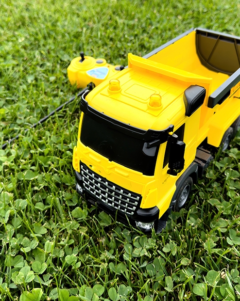 Overhead view of a radio-controlled play truck with a remote sitting next to it on the green lawn of a backyard.