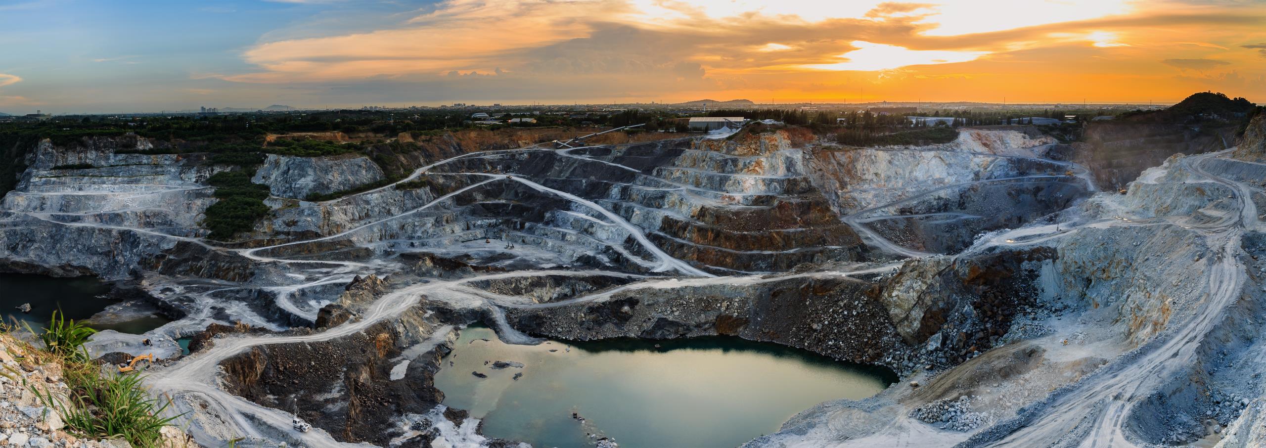 An aerial view of a mine highwall landscape with a sunset on the horizon