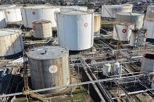 Industrial fuel storage facility with multiple large cylindrical tanks, interconnected pipelines, and processing equipment viewed from above.