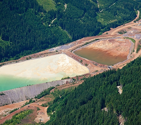 Aerial view of lined water containment ponds surrounded by forested mining operations.