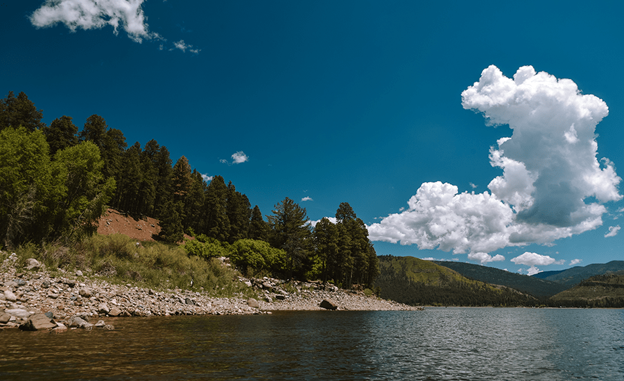 Rocky shoreline and forest beside a mountain lake.