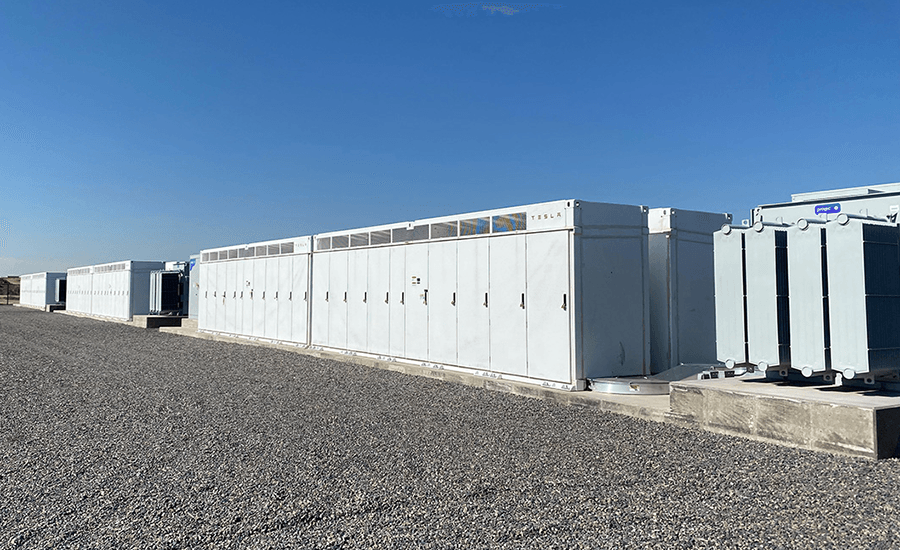 A row of large white industrial batteries on a concrete pad under a cloudless sky.
