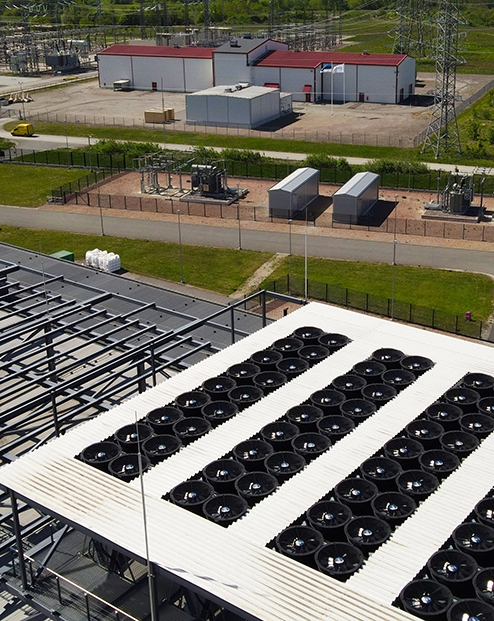 Aerial view of a data center rooftop with large cooling fans and adjacent electrical substation, highlighting power infrastructure, HVAC climate control, and industrial-scale operations.