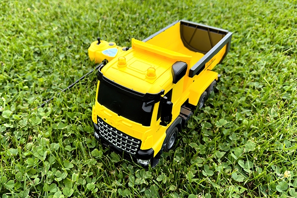 Overhead view of a radio-controlled play truck with a remote sitting next to it on the green lawn of a backyard.