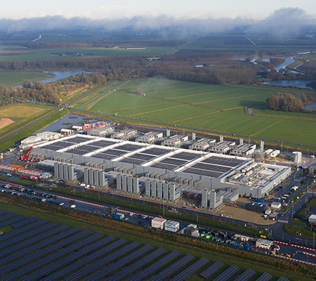 Large data center campus with ground mounted solar arrays powering sustainable cloud computing infrastructure in a green rural landscape, showcasing clean energy and tech growth.